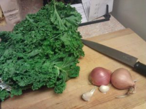 Picture of kale, shallots, garlic, and a chef's knife on a cutting board in my kitchen
