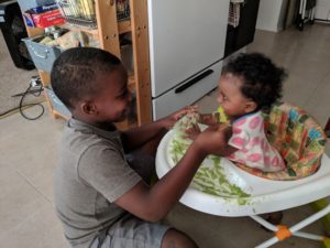 Picture of my son, Khaden, feeding his toddler cousin peas in a baby chair